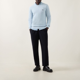 Model wearing Fred Perry Wreath Logo Sweater in Light Ice blue crew neck, styled with dark trousers and a collared shirt underneath.