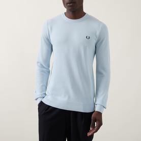 Model wearing Fred Perry Wreath Logo Sweater in Light Ice, crew neck cotton knit with ribbed trims and embroidered logo, styled with navy trousers