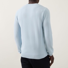Model wearing Fred Perry Wreath Logo Sweater in Light Ice, back view, crew neck, ribbed trims, styled with dark trousers.