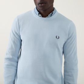 Model wearing Fred Perry Wreath Logo Sweater in Light Ice, crew neck cotton knit with embroidered logo, layered over a collared shirt.