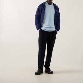 Model wearing Fred Perry Wreath Logo Sweater in Light Ice, styled with navy zip-up jacket, black trousers and chunky black shoes.