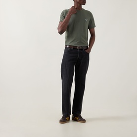 Model wearing Fred Perry Ringer Laurel Wreath T-Shirt in Laurel Wreath Green with dark jeans and brown shoes
