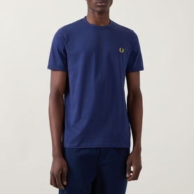 Model wearing Fred Perry Ringer Laurel Wreath T-Shirt in French Navy, crew neck with gold Laurel Wreath chest logo, paired with navy trousers.