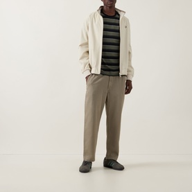 Model wearing Fred Perry Black Crew Neck T with bold dark stripe pattern, styled with cream zip jacket and taupe trousers.