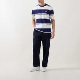 Model wearing Fred Perry Heavy-Striped Laurel Wreath Logo T-Shirt in Ecru with navy wide stripes, styled with navy trousers and white trainers.
