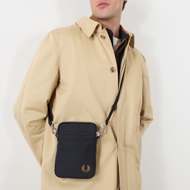 Model carrying Fred Perry Brentham Small Crossbody Bag in black with silver-tone hardware and embroidered Laurel Wreath logo, worn over beige coat
