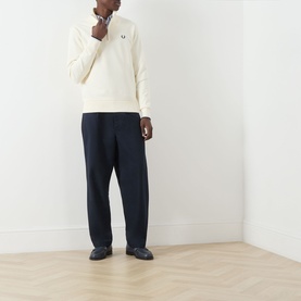 Model wearing Fred Perry Ecru Half Zip sweatshirt with navy trousers and dark slip-on shoes on herringbone wood floor.