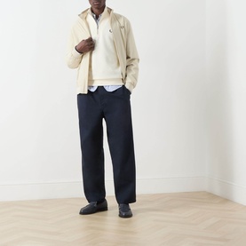 Model wearing Fred Perry Ecru Half Zip sweatshirt with navy trousers, light blue shirt, beige jacket and dark loafers.