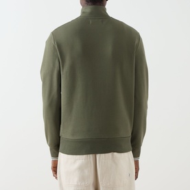 Model wearing Fred Perry Half Zip sweatshirt in Laurel Wreath Green, back view, with contrast tipped cuffs and hem, styled with ecru trousers.