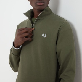 Model wearing Fred Perry Half Zip sweatshirt in Laurel Wreath Green with ecru zip and embroidered laurel wreath logo at chest.