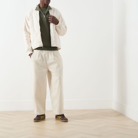 Model wearing Fred Perry Half Zip in Laurel Wreath Green, styled with ecru wide-leg trousers, matching jacket, and dark suede trainers.