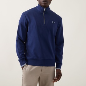 Model wearing Fred Perry Wreath Logo Half-Zip Sweatshirt in French Navy, with funnel neck and ribbed cuffs, styled with beige trousers.