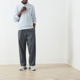 Model wearing Fred Perry Laurel Wreath Half-Zip Sweatshirt in Dusky Blue with grey trousers and white trainers.
