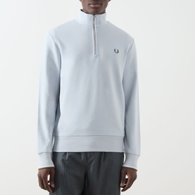 Model wearing Fred Perry Laurel Wreath Half-Zip Sweatshirt in Dusky Blue, with mock neck, half-zip and embroidered laurel wreath logo.