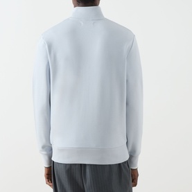 Model wearing Fred Perry Laurel Wreath Half-Zip Sweatshirt in Dusky Blue, back view, ribbed trims, styled with grey trousers.