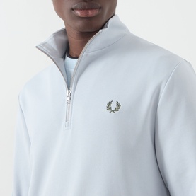 Model wearing Fred Perry Laurel Wreath Half-Zip Sweatshirt in Dusky Blue with embroidered laurel wreath logo and half-zip mock neck