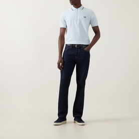 Model wearing Fred Perry Laurel Logo Crepe Piqu&eacute; Polo Shirt in Light Ice with dark rinse jeans and canvas shoes.