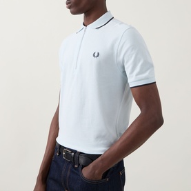 Model wearing Fred Perry Laurel Logo Crepe Piqu&eacute; Polo Shirt in Light Ice with navy twin tipping and chest Laurel Wreath logo, styled with dark jeans
