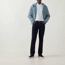 Model wearing Fred Perry Laurel Logo Crepe Piqu&eacute; Polo Shirt in Light Ice, styled with a blue jacket, dark jeans and navy trainers.