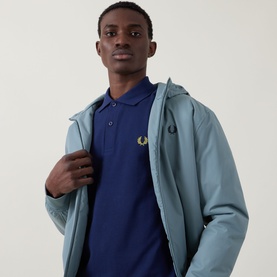 Model wearing Fred Perry Twin Tipped Polo Shirt in French Navy/Citron, styled under a light blue zip-up jacket.