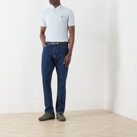 Model wearing Fred Perry Twin Tipped Polo Shirt in Dusty Blue with dark navy jeans and grey trainers.