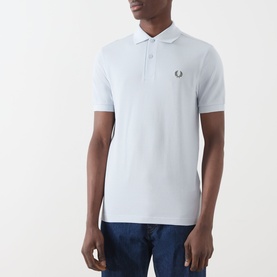 Model wearing Fred Perry Twin Tipped Polo Shirt in Dusty Blue with Laurel Wreath Green tipping, short sleeves, chest logo, styled with blue jeans.