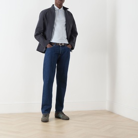 Model wearing Fred Perry Twin Tipped Polo Shirt in Dusty Blue, styled with dark grey jacket, navy jeans and grey trainers.
