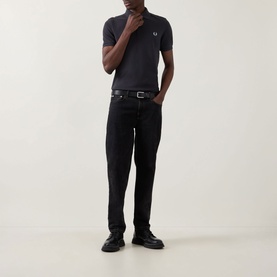 Model wearing Fred Perry Twin Tipped Polo Shirt in Anchor Grey, styled with black jeans and black leather shoes.