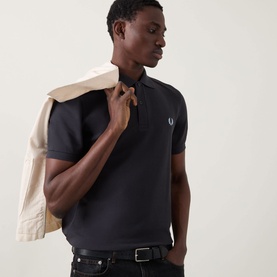 Model wearing Fred Perry Twin Tipped Polo Shirt in Anchor Grey, with cream jacket draped over shoulder and black jeans.