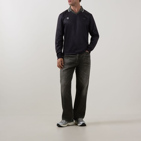 Model wearing Fred Perry Meyba Long-Sleeve Polo in Black with flat collar and laurel wreath logo, styled with dark jeans and grey trainers.