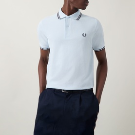 Model wearing light blue Fred Perry polo shirt with navy tipped collar and cuffs, styled with navy trousers