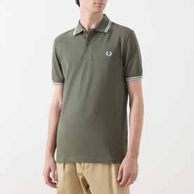 Model wearing Fred Perry Twin Tipped Logo Polo Shirt in Laurel Wreath Green with Ecru and Dusky Blue tipped collar and cuffs.