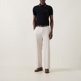 Model wearing Fred Perry Laurel Logo Twin Tipped Polo Shirt in Black/Oatmeal, styled with cream wide-leg trousers and brown loafers.