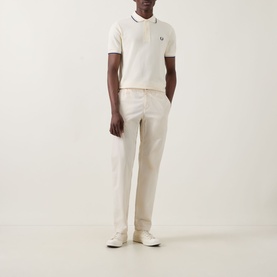 Model wearing cream knit polo shirt with navy tipping detail and small chest logo, styled with matching cream trousers and white trainers