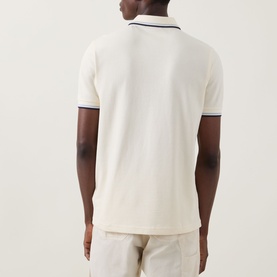 Model wearing cream polo shirt with navy tipping on collar and cuffs, styled with light beige trousers, rear view