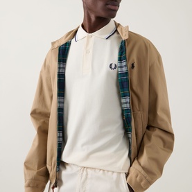 Model wearing a camel zip-up harrington jacket with plaid lining, styled with a white polo shirt and cream trousers.