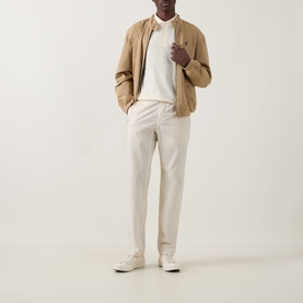 Model wearing a tan zip-up bomber jacket with cream polo shirt, stone chino trousers and white trainers