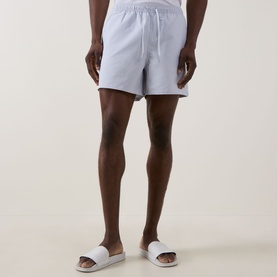 Model wearing Fred Perry Laurel Logo Swim Shorts in Dusky Blue with elasticated drawstring waist, styled with white slider sandals
