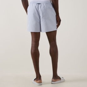 Model wearing Fred Perry Laurel Logo Swim Shorts in Dusky Blue, rear view, styled with white slide sandals