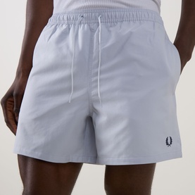 Model wearing Fred Perry Laurel Logo Swim Shorts in Dusky Blue with elasticated drawstring waist and embroidered Laurel Wreath logo.