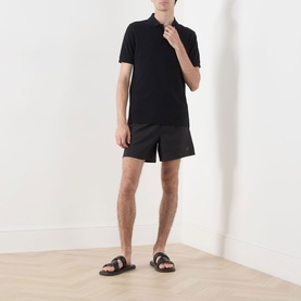 Model wearing Fred Perry Laurel Wreath Swim Shorts in black with a black polo shirt and black slider sandals.