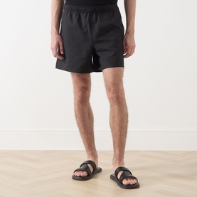 Model wearing Fred Perry Laurel Wreath Swim Shorts in black with elasticated waistband, styled with black slide sandals