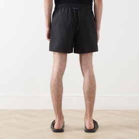 Model wearing Fred Perry Laurel Wreath Swim Shorts in black with elasticated drawstring waist, shown from behind with dark sandals.