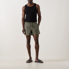 Model wearing Fred Perry Laurel Logo Swim Shorts in Laurel Wreath Green with black vest top and brown slides.