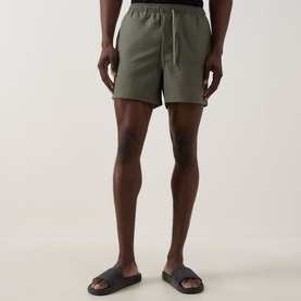 Model wearing Fred Perry Laurel Logo Swim Shorts in Laurel Wreath Green with elasticated drawstring waist, styled with black slider sandals.