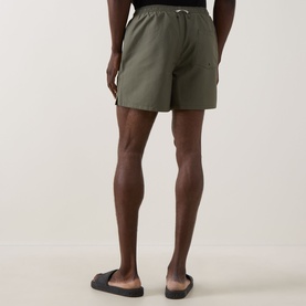 Model wearing Fred Perry Laurel Logo Swim Shorts in Laurel Wreath Green, rear view, with black slider sandals.