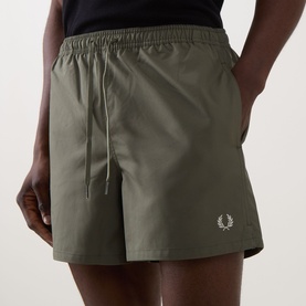 Model wearing Fred Perry Laurel Logo Swim Shorts in Laurel Wreath Green with elasticated waistband, drawstring, and embroidered logo. Styled with