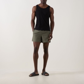 Model wearing Fred Perry Laurel Logo Swim Shorts in Laurel Wreath Green with black vest and dark slide sandals.