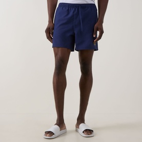 Model wearing Fred Perry Laurel Logo Swim Shorts in French Navy with white slider sandals. Elasticated waistband with drawstring.