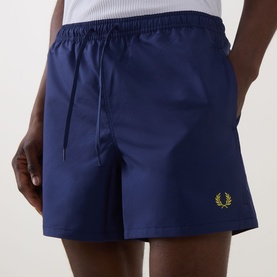 Model wearing Fred Perry Laurel Logo Swim Shorts in French Navy with gold Laurel Wreath logo, elasticated drawstring waist, straight-leg cut
